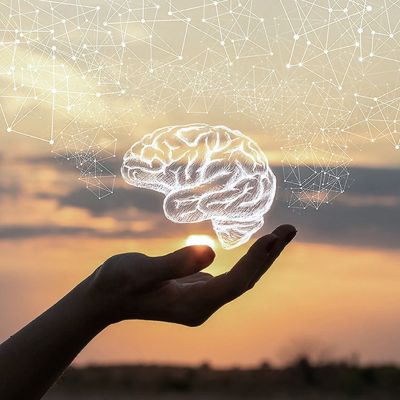 Hand holding a glowing, semi-transparent brain against a sunset backdrop with interconnected lines and nodes above it.